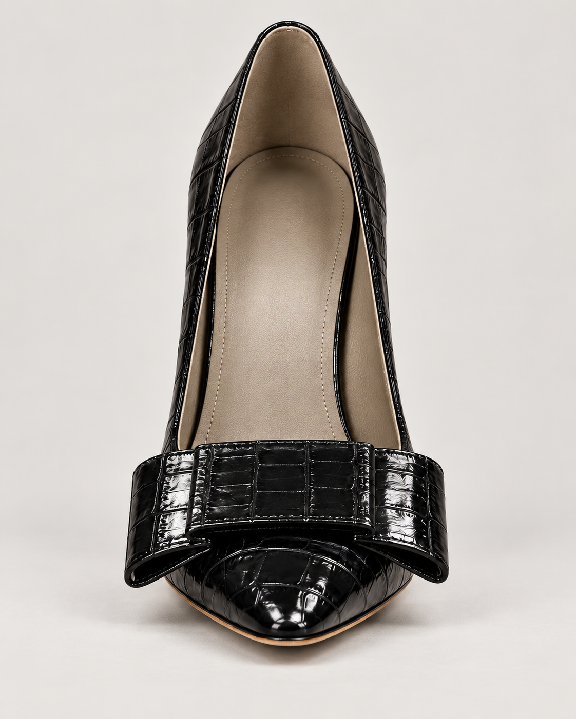 Front view of the glossy black croc-effect pump, showing its pointed toe, broad bow and beige interior.