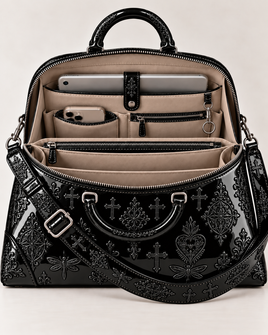 Open view of the shiny black patent leather handbag, showing beige interior compartments, device pockets, zipped storage and a key ring.