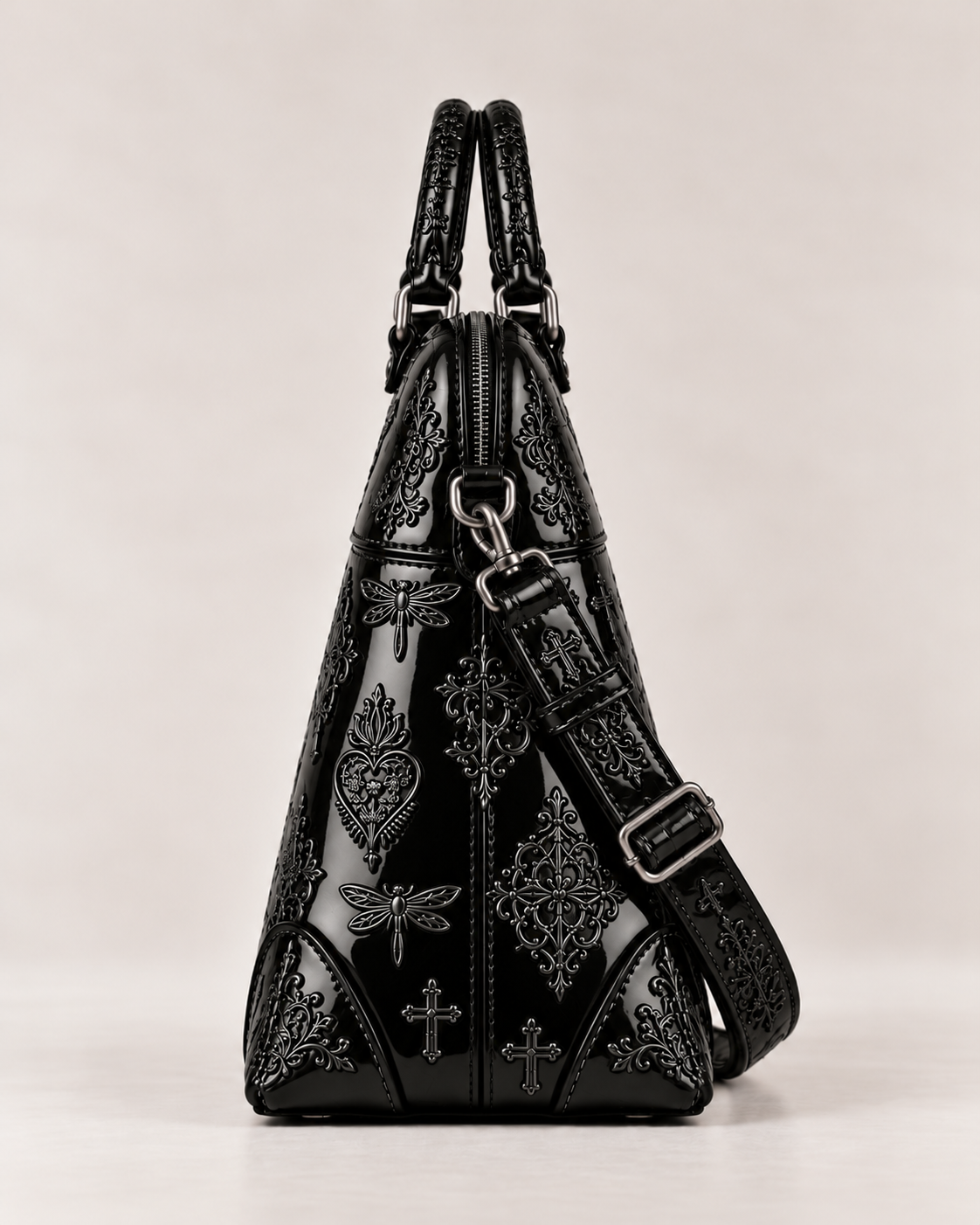Side view of the shiny black patent leather embroidered handbag, showing its structured shape, top zip and strap attachment.