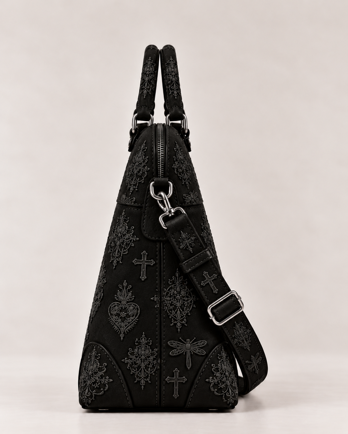 Side view of the black embroidered structured handbag, showing its tapered shape, top zip and detachable strap attachment.