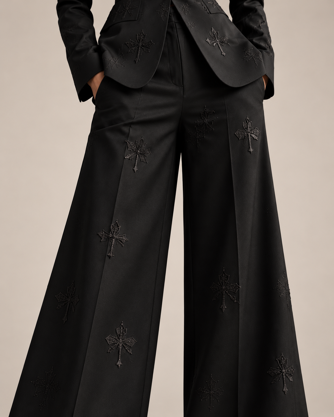 Close-up of the black silk satin trousers, showing the pockets, pressed creases and tonal cross embroidery.