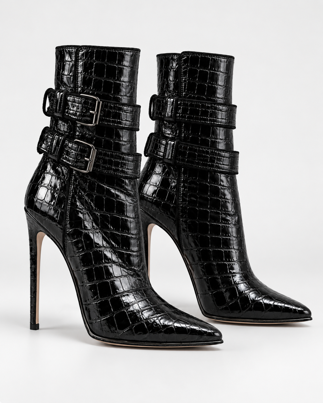 Three-quarter view of the black PLIS D’OMBRE croc-effect double-buckle ankle boots, with pointed toes, glossy textured uppers and stiletto heels.