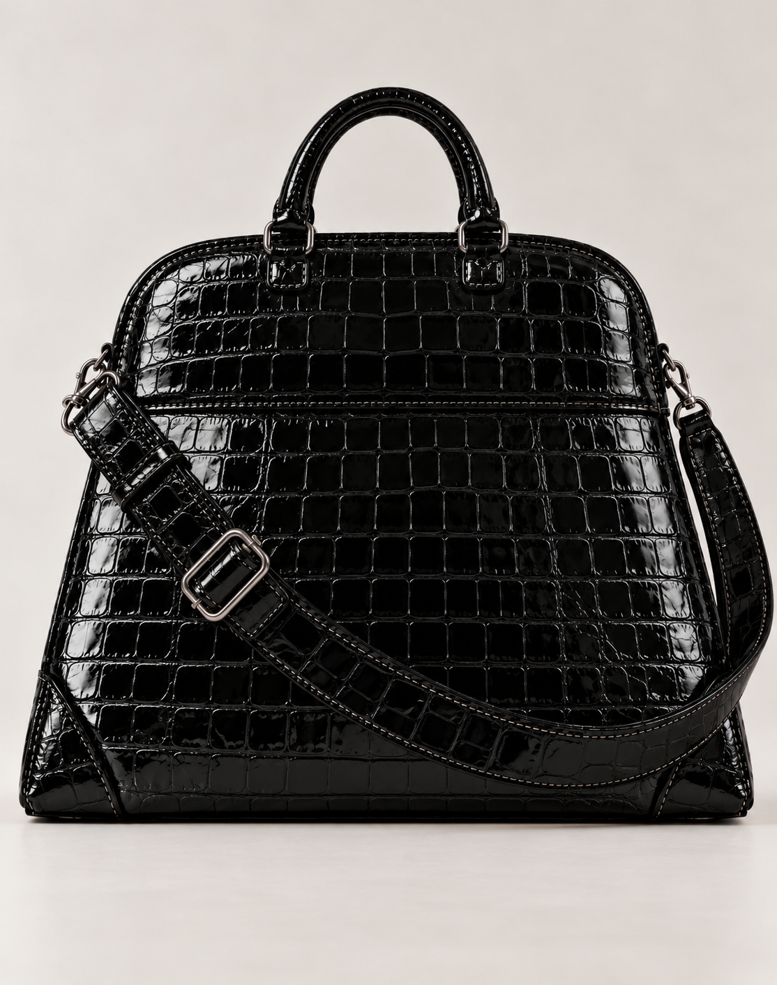 Front view of the black PLIS D’OMBRE croc-effect structured handbag, showing rounded handles, a glossy textured finish and an adjustable shoulder strap.