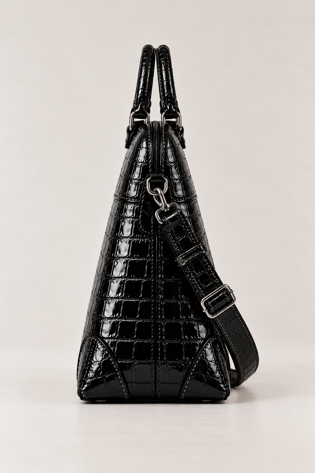 Side view of the black croc-effect structured handbag, showing its tapered shape, top zip and detachable shoulder strap attachment.