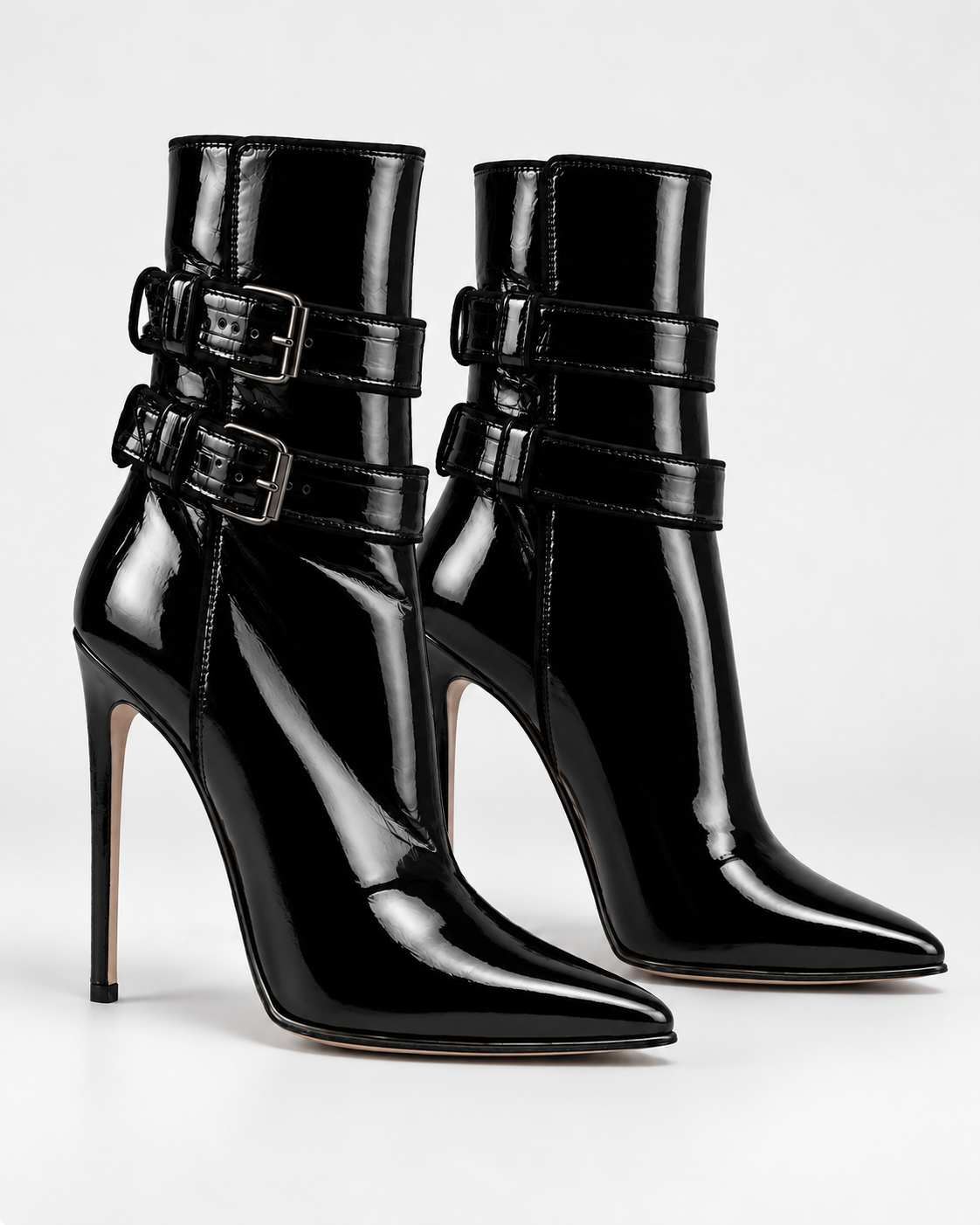 Three-quarter view of the black PLIS D’OMBRE glossy double-buckle ankle boots, showing pointed toes and stiletto heels.